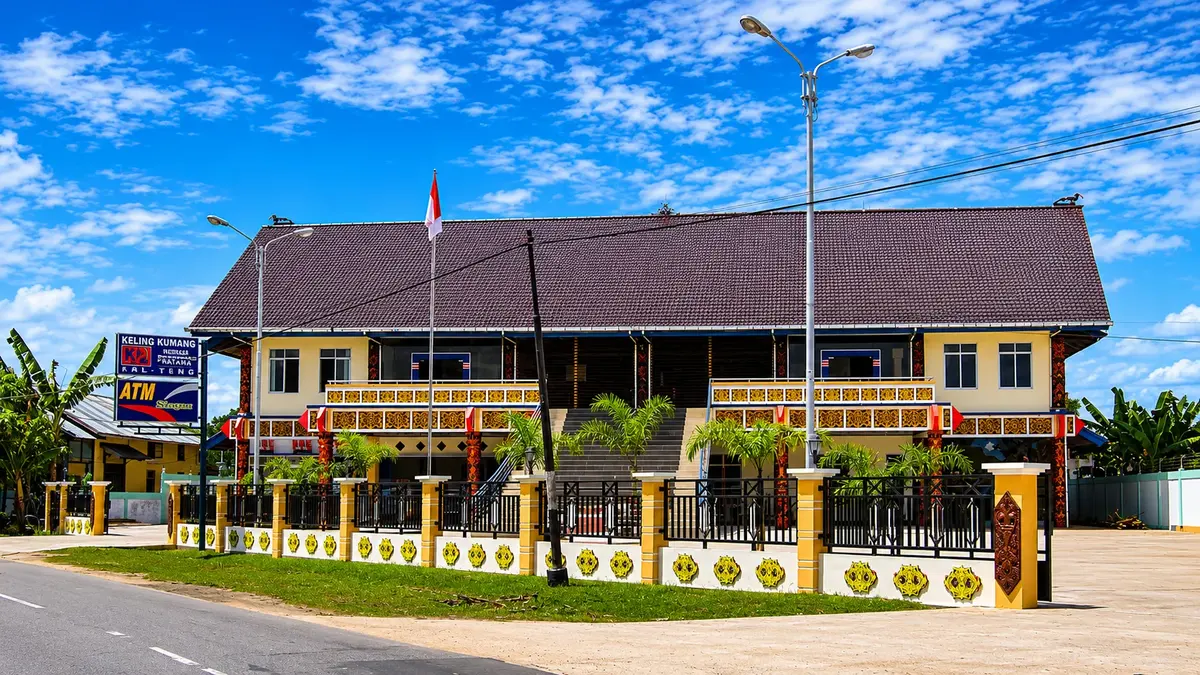 Gedung Gerakan Keling Kumang (GKK) bergaya rumah panjang Dayak dengan ornamen khas berwarna emas, berdiri di tepi jalan di Kalimantan Tengah, melambangkan ekosistem koperasi yang dibangun dari akar budaya dan kebersamaan / The Keling Kumang Movement (GKK) building in the style of a Dayak longhouse with distinctive golden ornaments, standing by the roadside in Central Kalimantan, symbolising a cooperative ecosystem built from cultural roots and togetherness